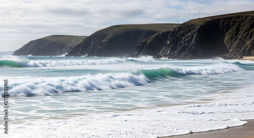 Ocean waves crashing on the shore with mountain cliffs in the background