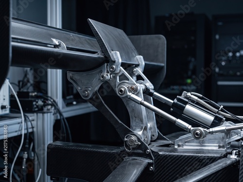 race car rear wing mechanism featuring carbon fiber construction and hydraulic actuators viewed in a professional engineering laboratory setting