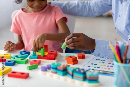 Happy Black Girl Playing With Brightly Colored Learning Blocks At Home, Engaging In Playful Activity With Adult Supervision, Enhancing Motor Skills And Cognitive Development. Family Concept.
