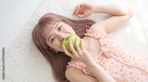 Plakat w ramie ラグの上に横になって青りんごを食べる若い女性