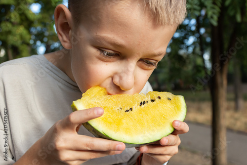 Canvas Print Portrait of a boy biting into a slice of yellow watermelon held in his hands