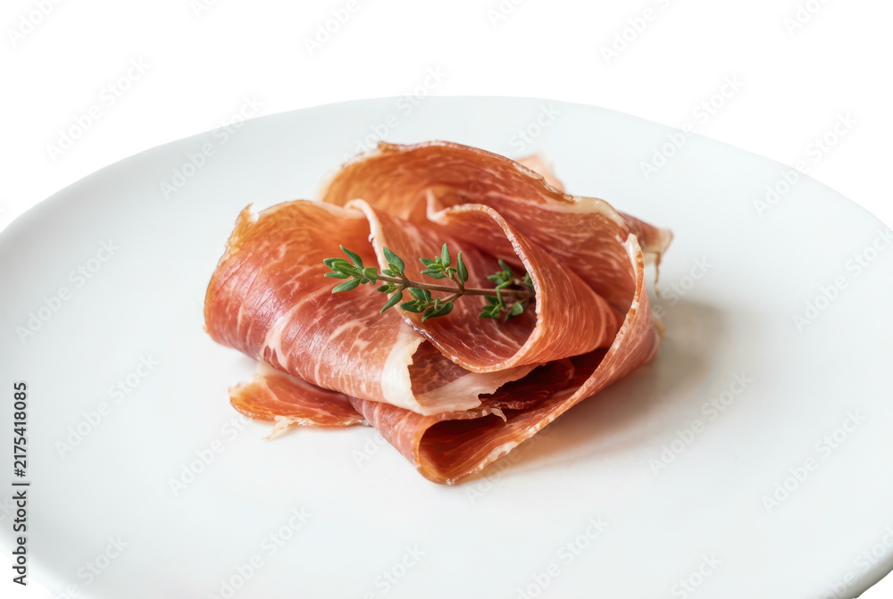 Fototapeta premium Thinly sliced cured pork meat folded on a white plate with fresh herbs