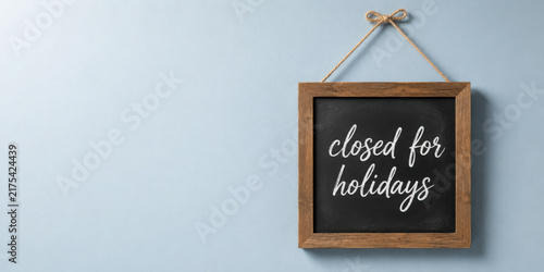 Closed for Holidays Sign. A simple, wooden framed chalkboard sign announces a business closure for the holidays against a light blue background.