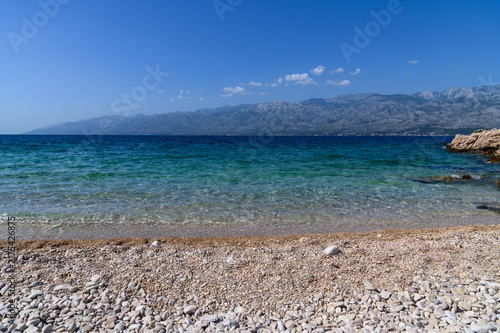 Pebble shore and clear Adriatic water at Bokulja beach below the barren Velebit mountains, Slivnica, Croatia