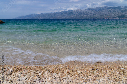 Smooth pebbles and gentle foam at the edge of a crystal clear turquoise sea on a summer beach