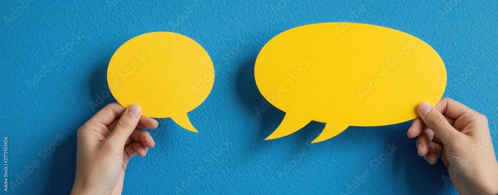 Naklejka premium Hands hold yellow speech bubbles against blue textured wall. Communication concepts like dialogue, ideas, conversation visually represented. Simple design for creative projects, social media posts.