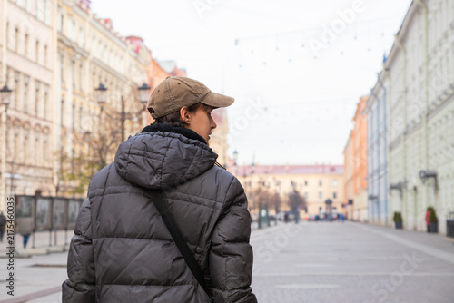 Man walking on empty city street. Young guy in cap and warm jacket strolling through old european town. Travel, urban lifestyle and autumn season concept.