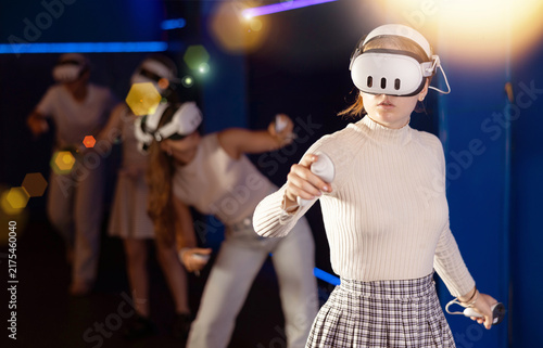 Obraz na płótnie Excited young girl in VR glasses interacting with immersive environment of virtual reality world, standing with controllers in hands and actively gesticulating while controlling objects in game
