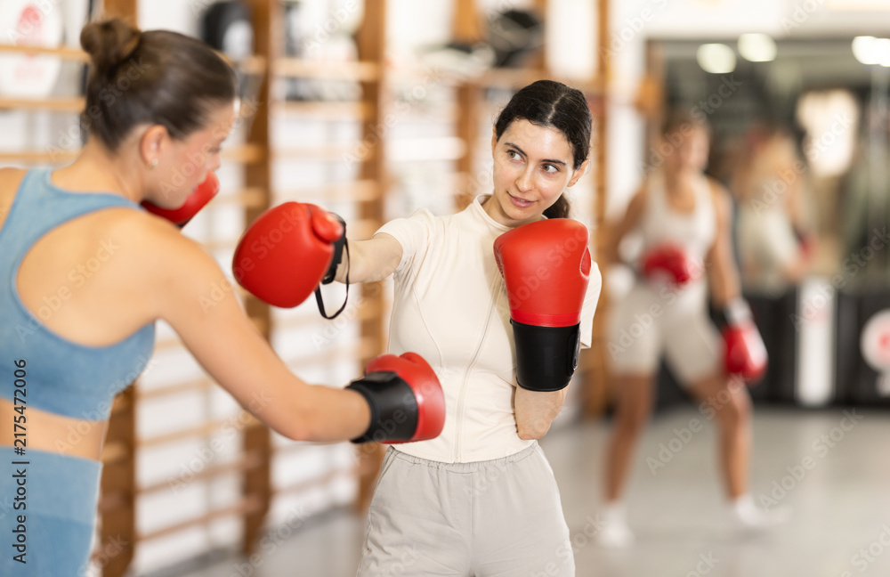Naklejka premium Two women in boxing gloves sparring together in the hall. Young women during group boxing training
