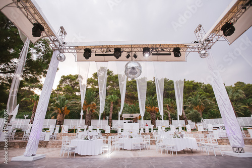 Fotografie Elegant Outdoor Event Setup: White draped tents and sparkling disco balls adorn an outdoor venue, setting the stage for a sophisticated celebration with elegantly set tables and chairs