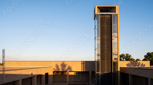 Tall glass solar chimney ventilation tower on contemporary building facade under clear blue sky.