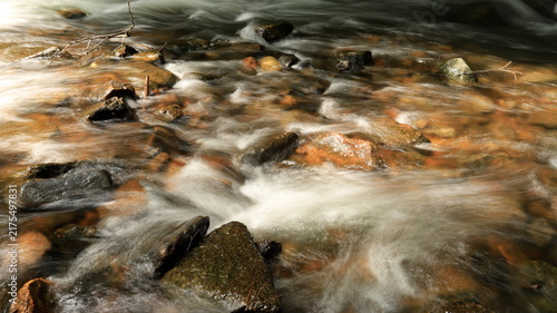 Close-up long exposure of silky river rapids flowing over colorful submerged stones and rocks