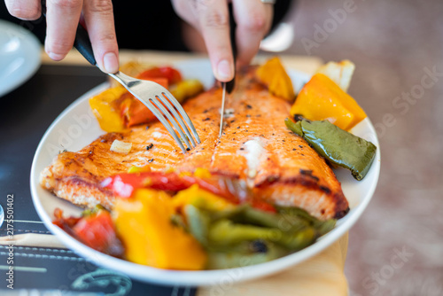 Canvas Print Person eating grilled salmon fillet with vegetables