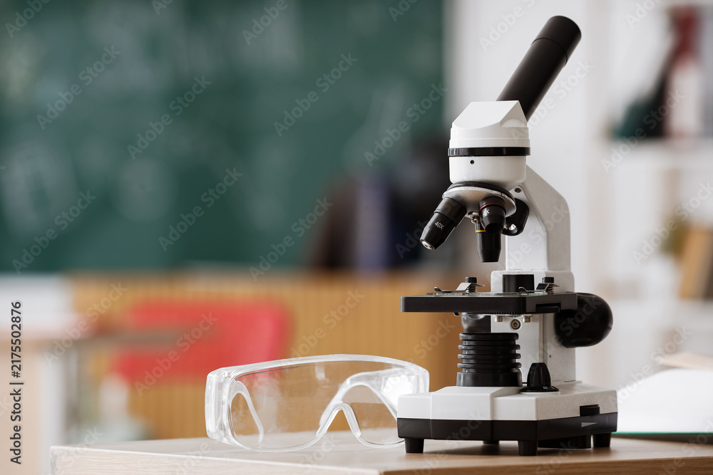 Naklejka premium Science education and research, microscope and safety goggles on a classroom desk for biology study and laboratory experiment in a school environment