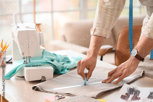 Fotografie Young male tailor with sewing machine marking cloth in atelier, closeup