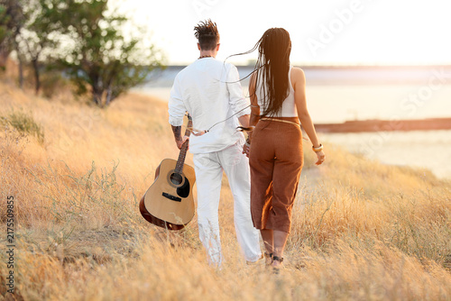 Young couple of hippies with dreadlocks and guitar outdoors, back view