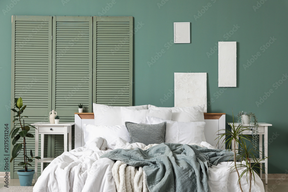 Naklejka premium Big comfortable bed, folding screen and bedside tables near green wall in bedroom, closeup