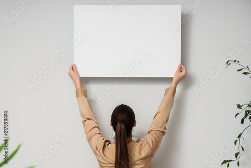 Young woman holding blank poster on white background, back view