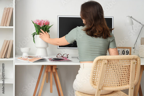 Young woman and vase with tulips on desk in home office, back view