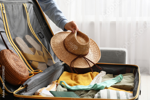 Young woman with hat packing suitcase for travel on sofa at home, closeup