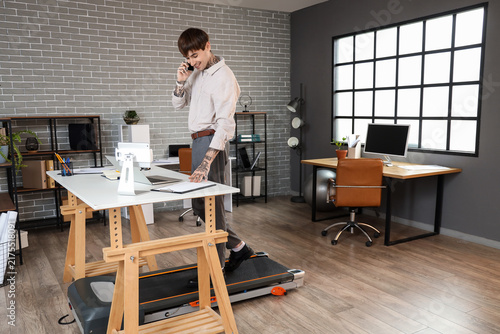 Handsome businessman talking by mobile phone on treadmill at table in office