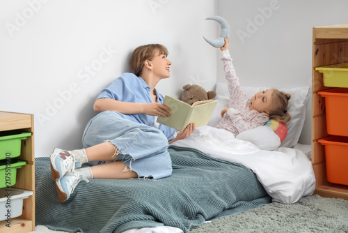 Nanny reading bedtime story to little girl in bedroom