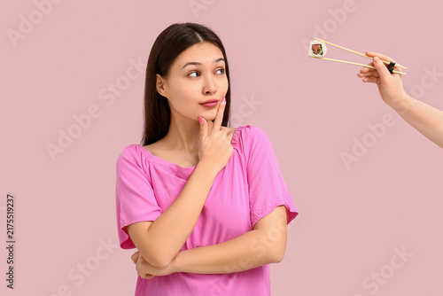 Thoughtful young Asian woman looking at female hand with tasty sushi roll on ...