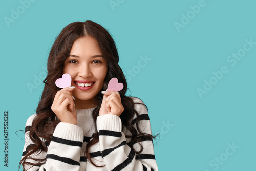 Happy young Asian woman with pink paper hearts on blue background. Valentines...