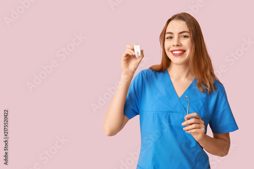 Female dentist with dental mirror and tooth model on pink background. World D...