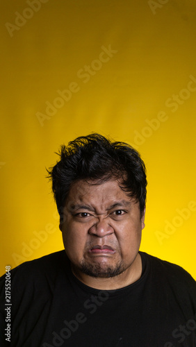 Cuadro en lienzo A highly displeased young Asian male tightly purses the lips and aggressively furrows the brow while staring straight ahead against a vivid solid yellow background