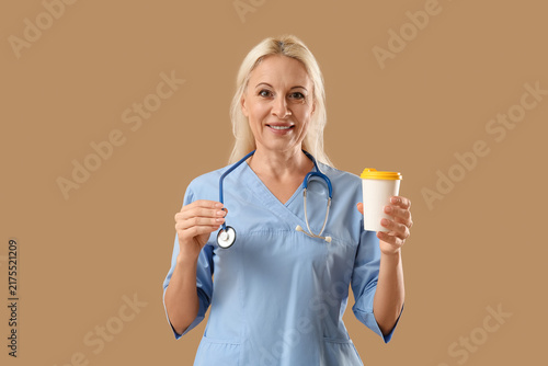 Mature female doctor with cup of coffee on brown background