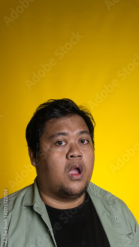 Foto An expressive young Asian male looks directly at the camera with a slightly open mouth and a surprised expression against a bright yellow background
