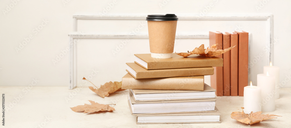 Obraz premium Cozy autumn reading and relaxation, paper coffee cup on a stack of books with dry leaves and candles for a peaceful home atmosphere and fall lifestyle