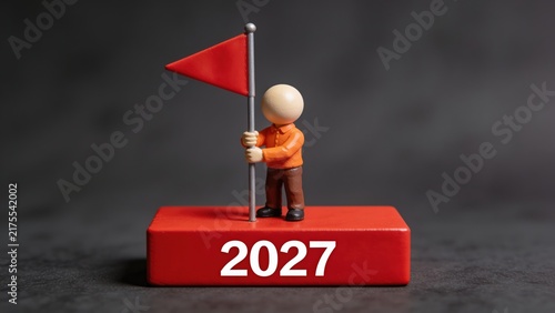Miniature Figure Holding Red Flag on 2027 Block Symbolizing New Year Goals and Achievement

