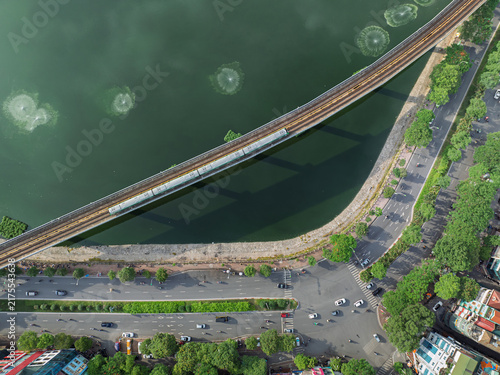 Aerial view of metro train crossing Dong Da Lake beside busy roads in Hanoi, Vietnam