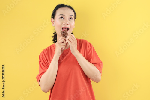 Quadro su tela A young Asian woman with a radiant smile enjoys a decadent bite of a chocolate b