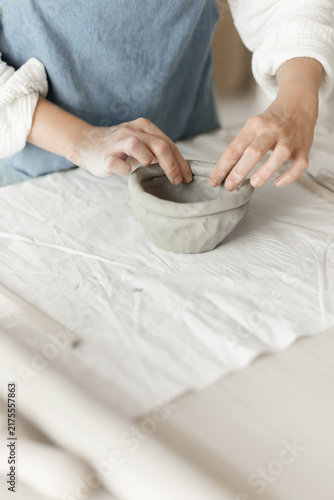 Woman potter meticulously shaping clay in a studio setting, demonstrating a creative and focused approach, captured in a close-up side view, the scene showcases.