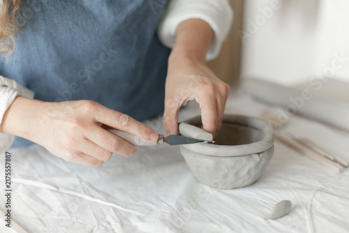 Woman potter meticulously shaping clay in a studio setting, demonstrating a creative and focused approach, captured in a close-up side view, the scene showcases.