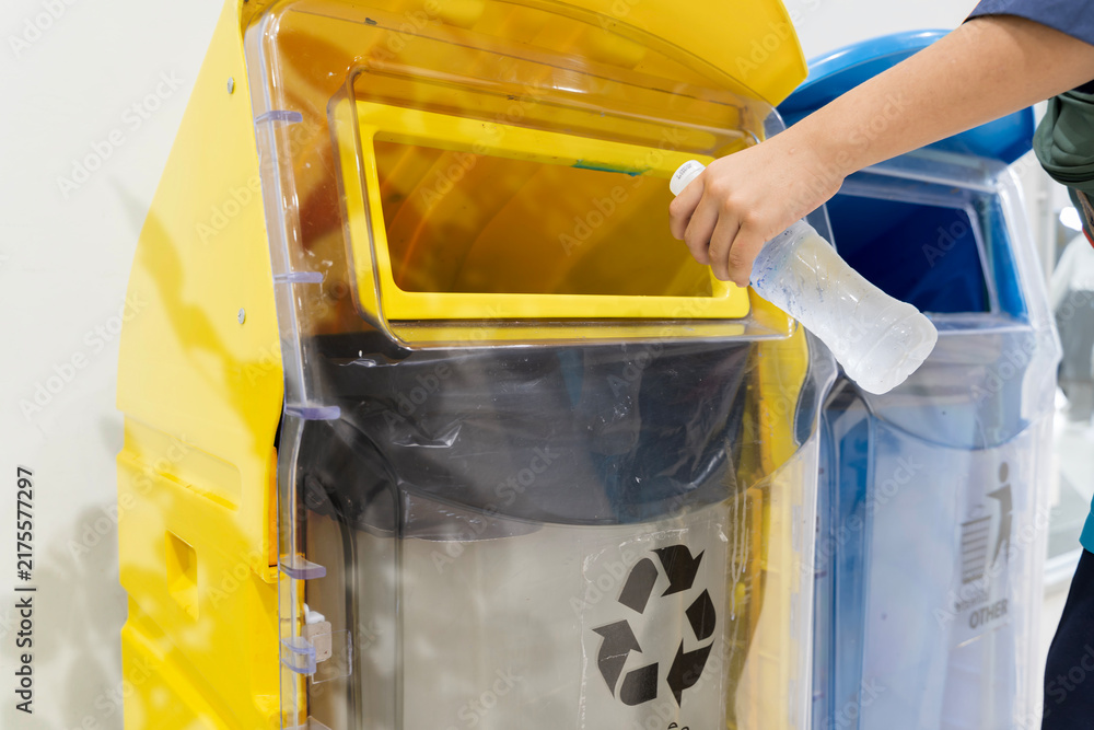 Obraz premium Hand Putting Plastic Bottle into Yellow Recycling Bin for Waste Management