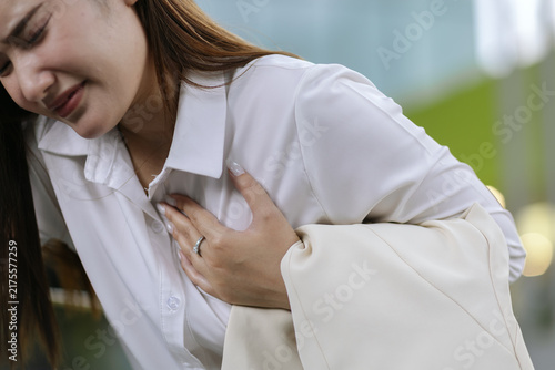 фотографія Businesswoman holding chest in discomfort at workplace, representing sudden pain, stress, fatigue, health concern, employee wellness and occupational healthcare concept