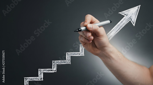 Hand drawing upward arrow and staircase on dark background