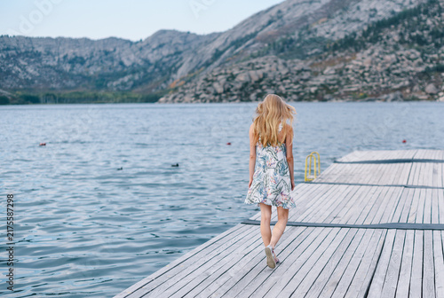 Rear view of blonde woman in floral dress walking on wooden pier at Sibiny Lakes East Kazakhstan