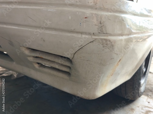 A detailed close up view of a damaged white car bumper showing cracks, scratches, and rust stains, highlighting vehicle body damage, collision repair work, and automotive maintenance.