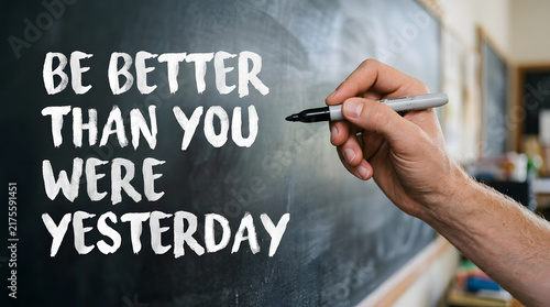 Hand writing motivational phrase on blackboard in classroom setting