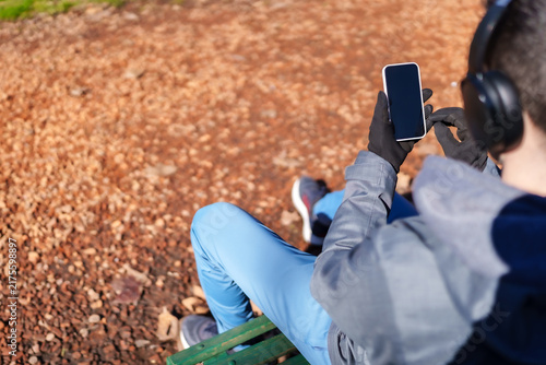 Man relaxing on park bench using smartphone and headphones