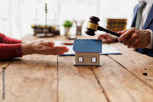 Foto Hand holding a gavel above a house model on a wooden table, symbolizing a proper