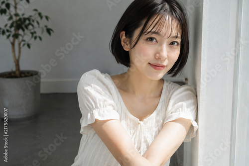 Plakat 明るい窓辺で白いパフスリーブブラウス姿の女性が腕を前で組んで微笑む