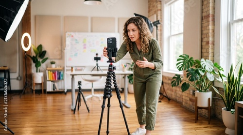 Social media manager filming video content with smartphone on tripod in home office studio