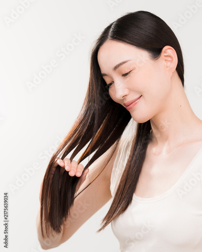 手ぐしで髪のお手入れをする黒髪ストレートヘアの日本人女性。ヘアケアイメージ。