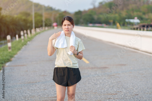 Foto Exhausted Asian woman wiping sweat with a towel after jogging in the park